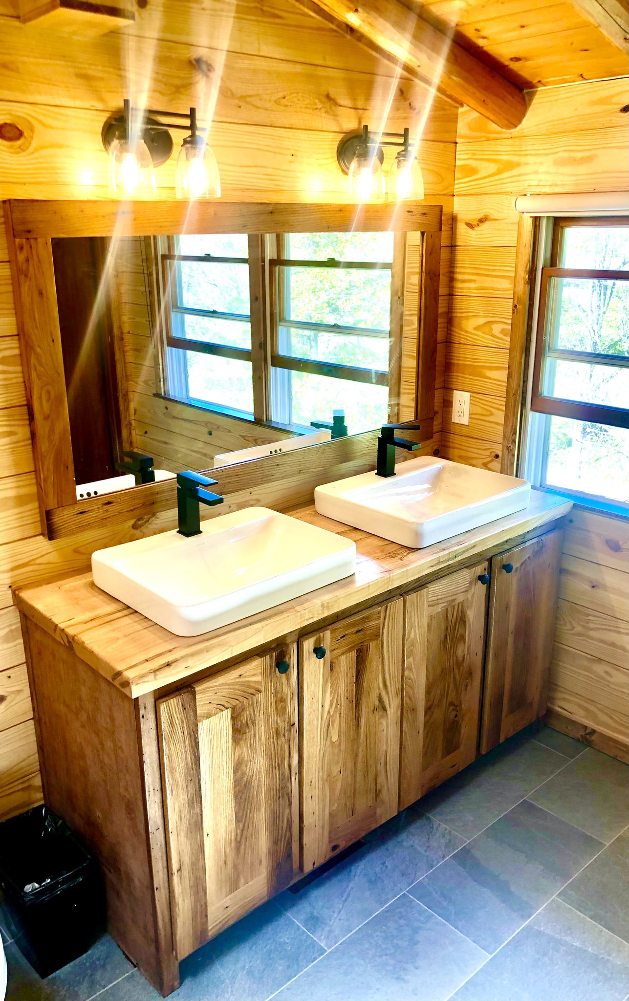 Custom rustic double bathroom vanity with reclaimed wood, vessel sinks, and black hardware in a log cabin